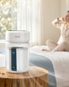 White cylindrical air purifier on a nightstand with blue-lit top display